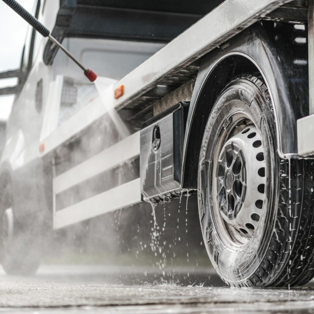 A person with a power washer spraying the wheels and underside of a commercial truck